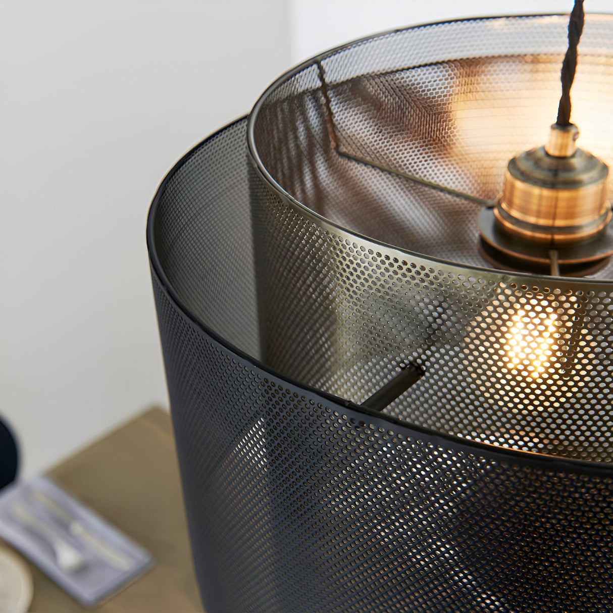 Chartfield Pendant close-up showing perforated black outer shade and antique brass inner cylinder with visible E27 lampholder and lit bulb.