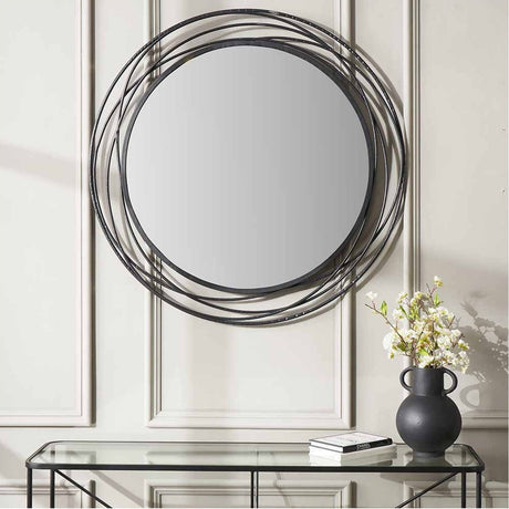 Black Iron Swirl Round Wall Mirror, 90 x 90cm, with layered black metal rings framing the glass, hung above a glass console table with a dark vase and books.