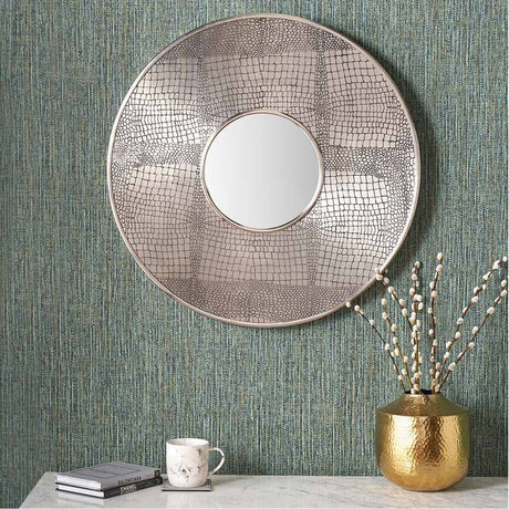 Round wall mirror with antique silver textured iron frame and small central mirror glass, shown on a green textured wall above a marble console with a gold vase.