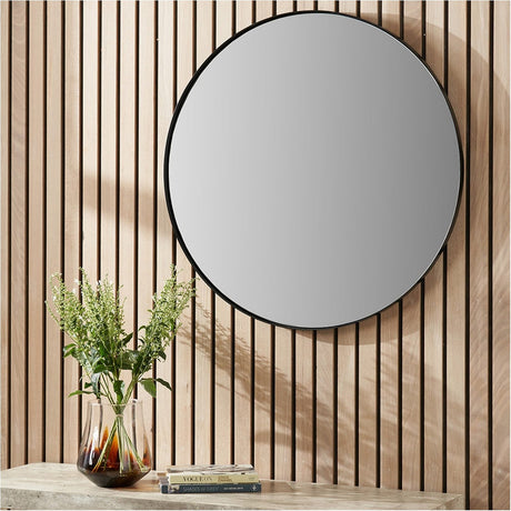 Slim Frame Black Stainless Steel Medium Round Wall Mirror, 80 x 80cm, mounted on a wood-slatted wall above a console table with a glass vase and books.