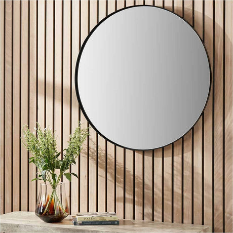 Round wall mirror with a slim black stainless steel frame, 60 x 60cm, mounted on a wood-slatted wall above a console table with a vase of flowers.