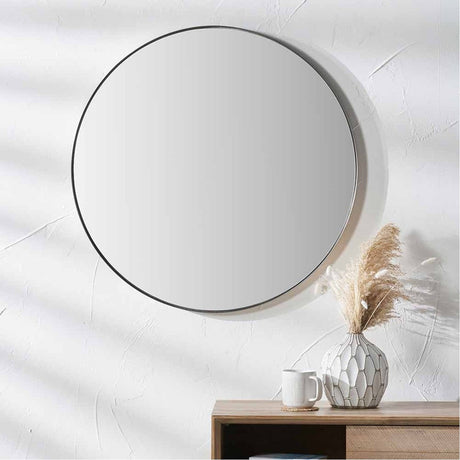 Round wall mirror with a slim brushed silver metal frame, 60 x 60cm, hung above a wooden console table with a vase and mug in a living room setting.