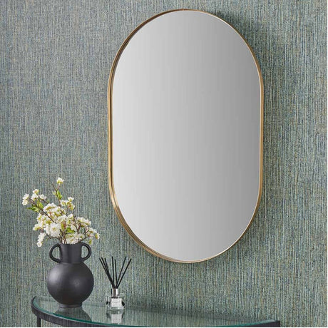 Slim frame brushed gold oval wall mirror, 60 x 90cm, hung above a glass console table with a black vase and dried florals against a textured teal wall.
