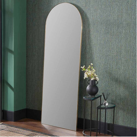 Slim frame brushed gold arch floor mirror, 70 x 200cm, leaning against a green textured wall in a hallway beside black side tables and a vase.