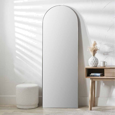 Slim frame brushed silver arch floor mirror, 70 x 200cm, leaning against a white wall beside a wooden console table and stool.