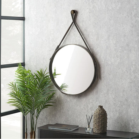 Round wall mirror with dark steel frame and leather hanging strap, styled above a black sideboard with a plant and decorative vase in a grey-walled hallway.