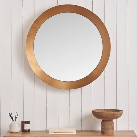 Round wall mirror with an angled burnished gold aluminium frame, 80 x 80cm, shown on a white panelled wall above a wooden console with decor.