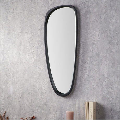 Black wood veneer teardrop-shaped wall mirror, 33 x 90cm, with asymmetric black frame, mounted on a grey textured wall above a shelf with books and a candle.