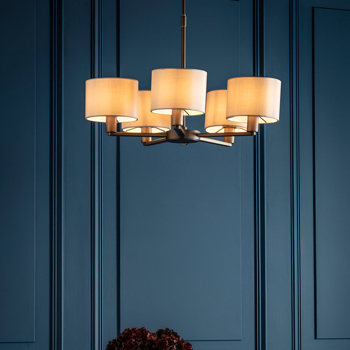 Endon Bexley 5 light pendant in bronze with marble-effect faux silk drum shades on curved arms, illuminated against a dark blue panelled wall.