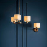 Endon Bexley single E14 wall light in bronze with a marble-effect faux silk drum shade, mounted on a panelled dark blue wall beside a matching chandelier.