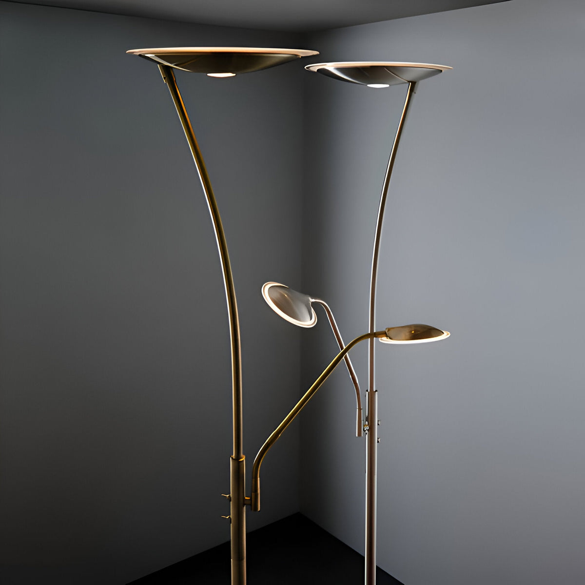 Endon Aldcombe LED floor lamps in antique brass and satin chrome, each with tall uplight dish and adjustable reading arm, shown in a grey corner.
