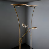 Endon Aldcombe LED floor lamps in antique brass and satin chrome, each with tall uplight dish and adjustable reading arm, shown in a grey corner.