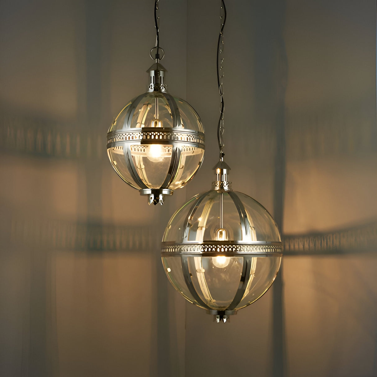 Two Endon Danecombe spherical pendant lights in nickel plated brass with clear glass globes, suspended from chains against a softly lit neutral background.