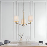 Endon Castwell 3 light pendant in antique brass with vintage white faux silk shades, hung above a dining table against panelled white walls.
