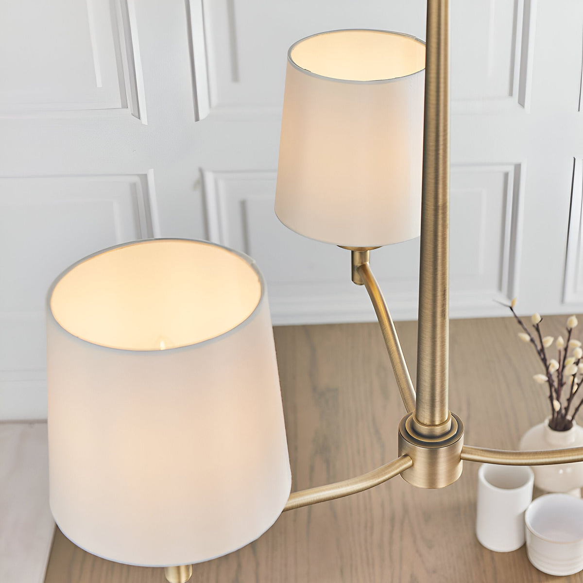 Close-up of the Endon Castwell 3 Light Pendant showing two lit vintage white fabric shades on curved antique brass arms in a panelled room.