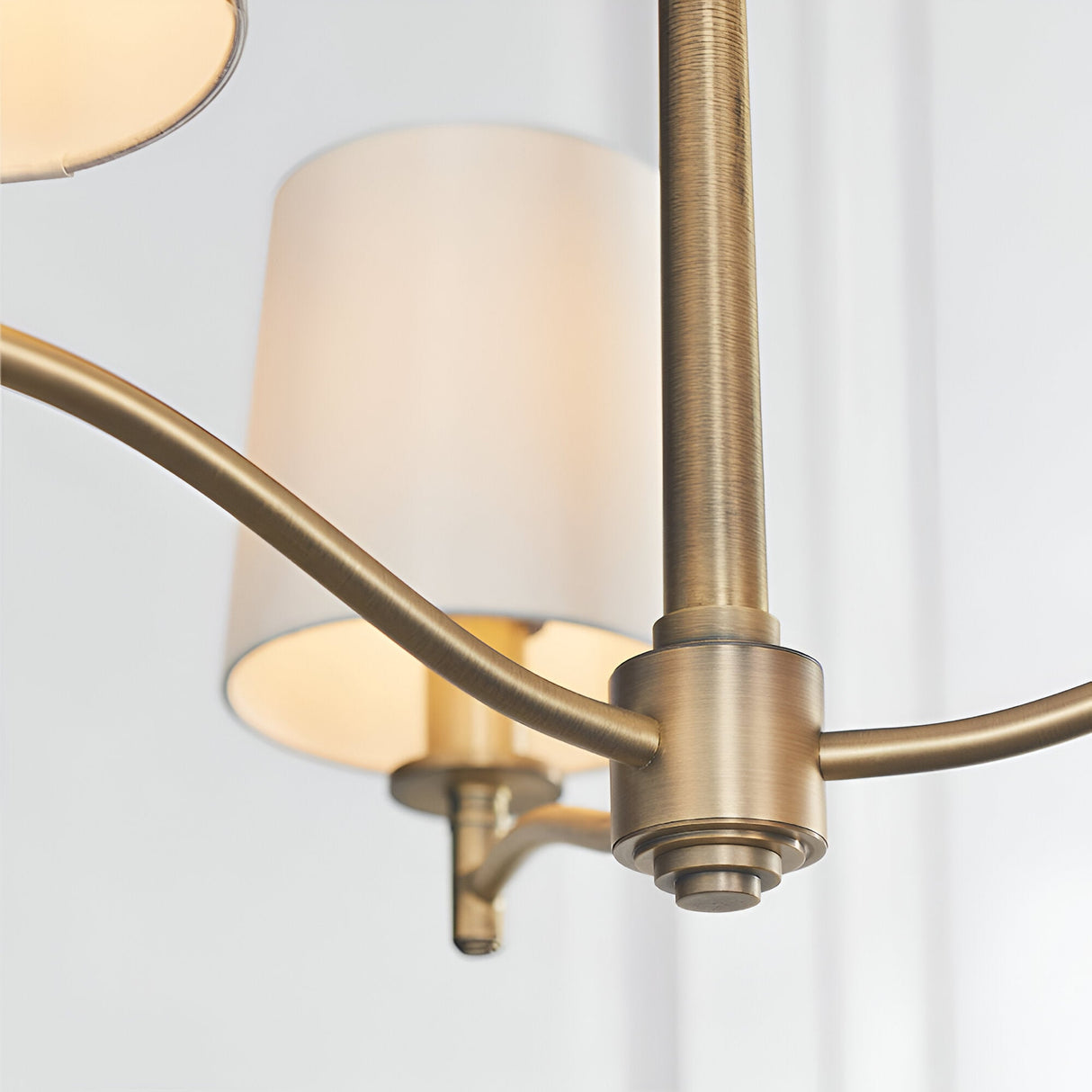 Close-up of Endon Castwell 3 Light Pendant showing matt antique brass arms and central stem with vintage white faux silk cylindrical shades.