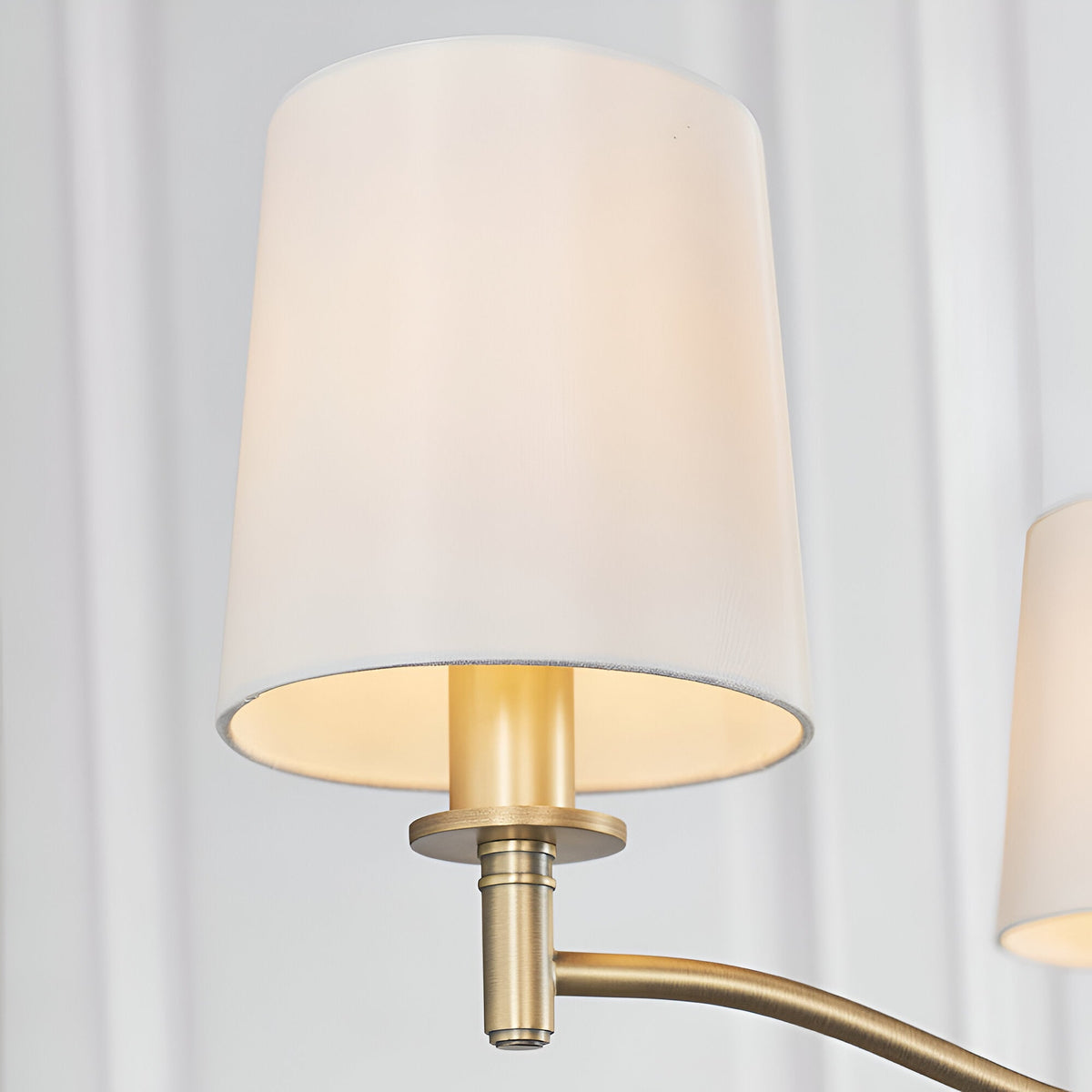Close-up of the Endon Castwell 3 Light Pendant showing a vintage white faux silk shade on a matt antique brass arm against a pale draped background.