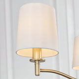 Close-up of the Endon Castwell 3 Light Pendant showing a vintage white faux silk shade on a matt antique brass arm against a pale draped background.