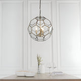 Endon Carldon 3 light pendant in antique brass with hexagonal clear glass panels, hung from a chain above a dining table against white panelled walls.