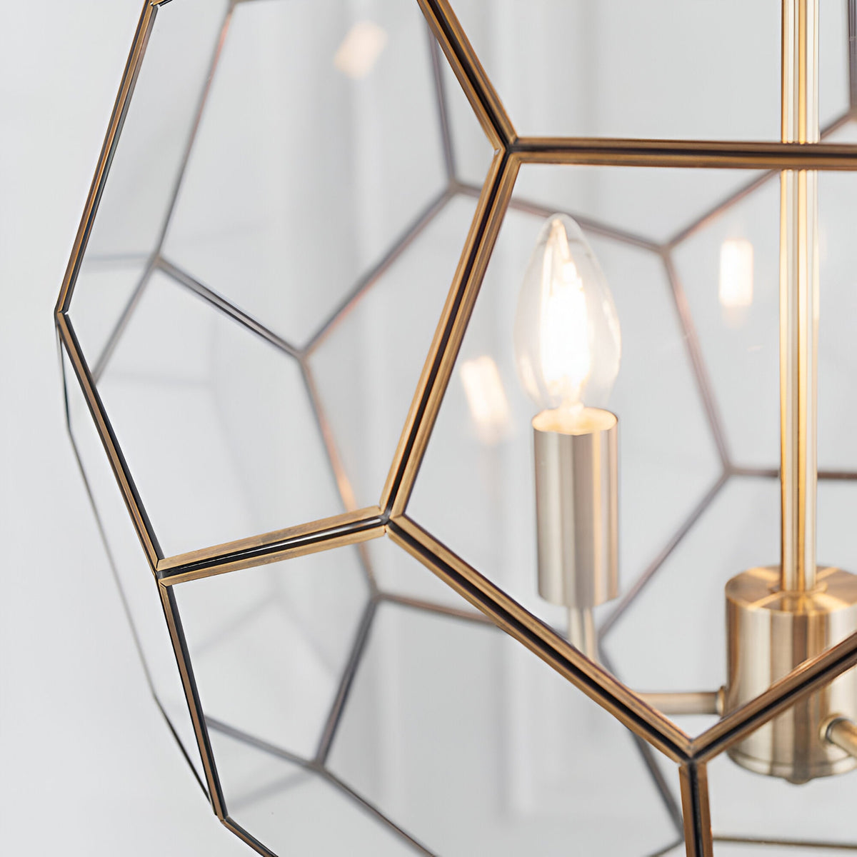 Close-up of Endon Carldon 3 Light Pendant in antique brass with hexagonal clear glass panels and a lit E14 candle bulb on a brass lampholder.