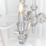 Close-up of Endon Brambourne 5 Light Pendant in polished aluminium, showing a candle-style E14 lampholder with lit bulb on a curved scrolled arm.
