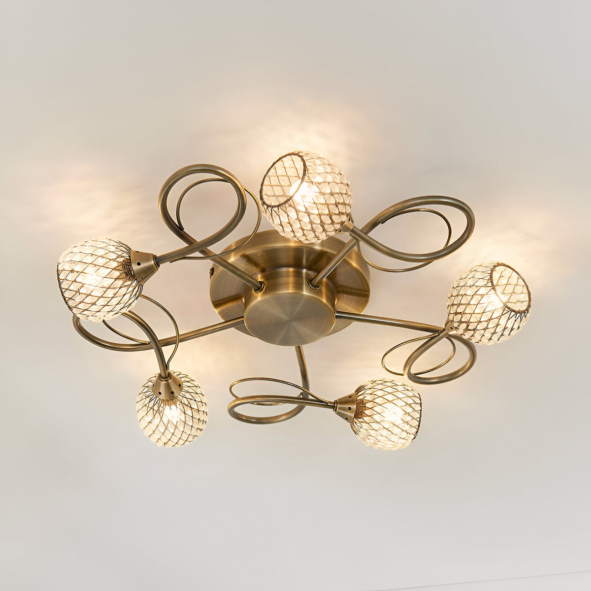 Endon Harcourt 5 light semi-flush ceiling light in antique brass with looped arms and mesh-caged glass globe shades, viewed from below.