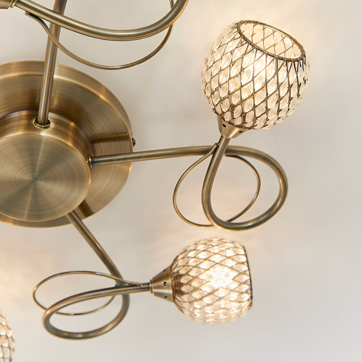 Close-up of the Endon Harcourt semi-flush ceiling light in antique brass, showing looped arms and mesh-caged glass globe shades lit warmly.