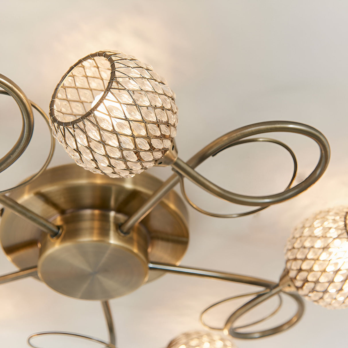 Close-up of Endon Harcourt 5 light semi-flush ceiling light in antique brass, showing looped arms and beaded mesh globe shades around a round base.