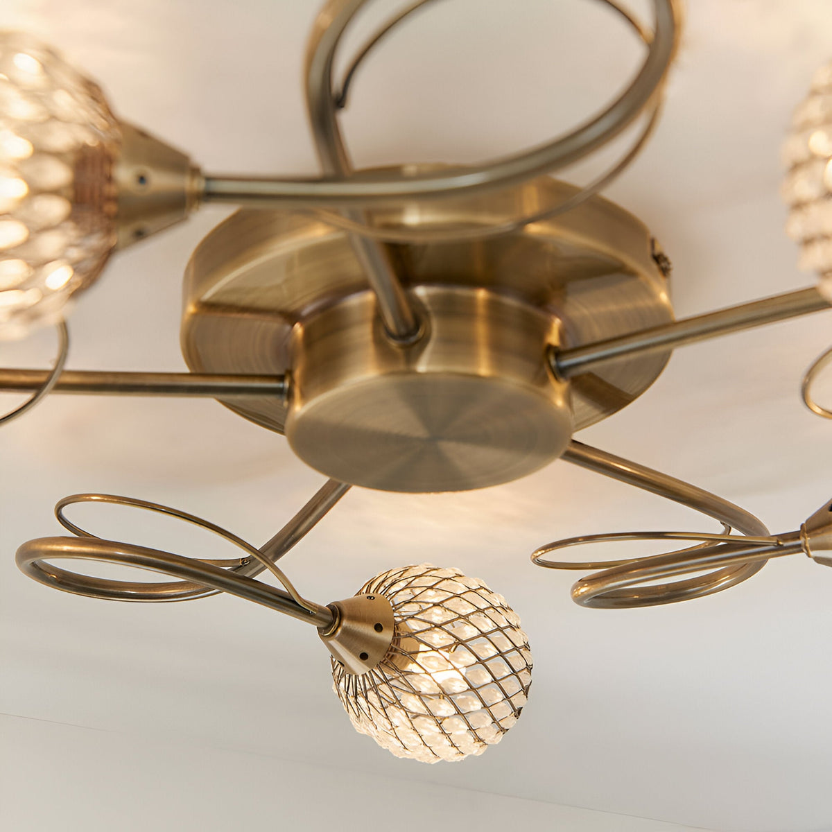 Close-up of the Endon Harcourt 5 Light Semi-Flush Ceiling Light in antique brass, showing curled arms and beaded glass globe shades.