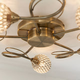 Close-up of the Endon Harcourt 5 Light Semi-Flush Ceiling Light in antique brass, showing curled arms and beaded glass globe shades.