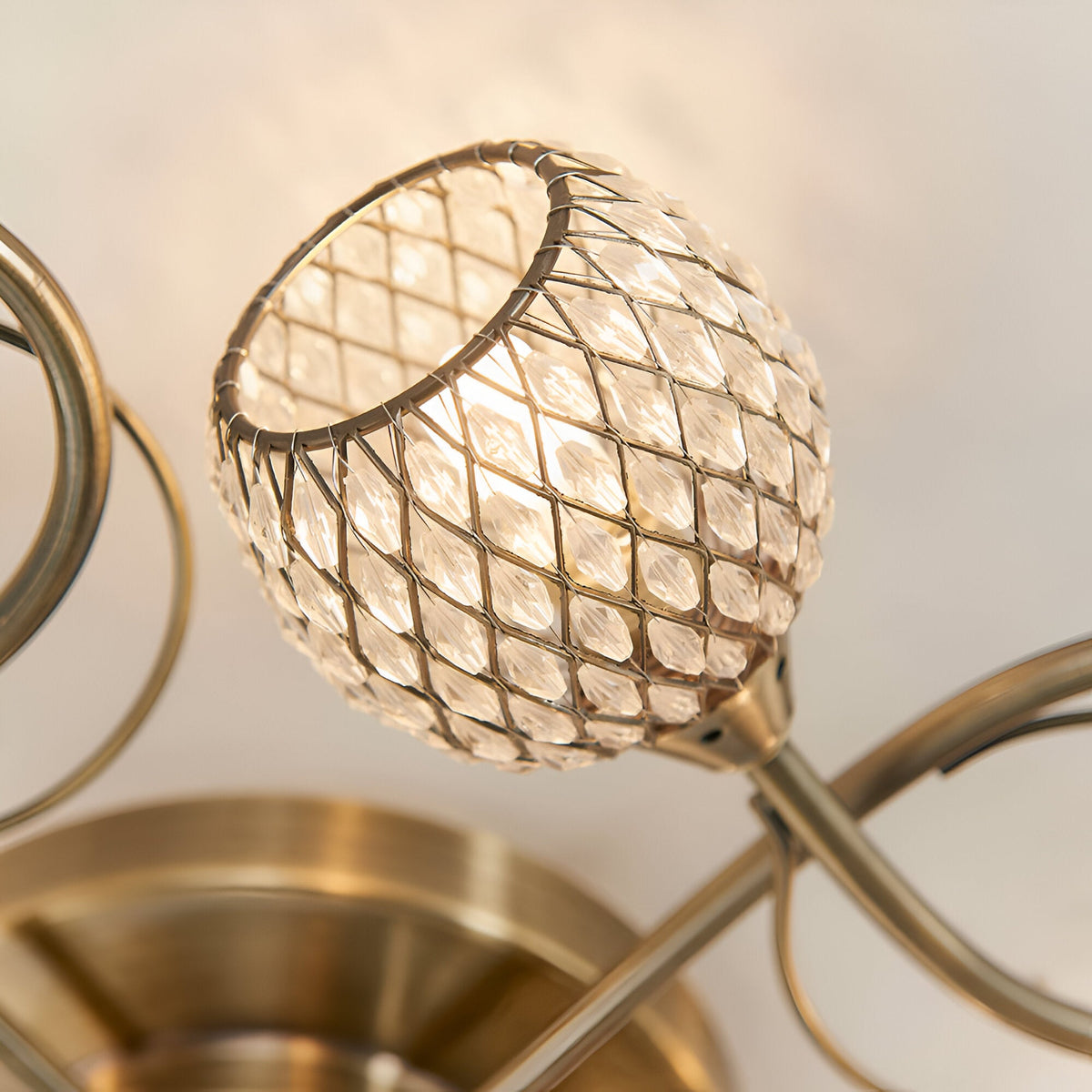 Close-up of one crystal-beaded globe shade on the Endon Harcourt 5 Light Semi-Flush Ceiling Light in antique brass, showing the curved arms.