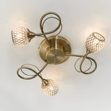 Endon Harcourt 3 light semi-flush ceiling light in antique brass, viewed from below showing curled arms and mesh-caged glass shades around a central disc.