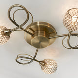 Close-up of the Endon Harcourt 3 light semi-flush ceiling light in antique brass, showing the central fitting, looped arms, and mesh crystal shades.