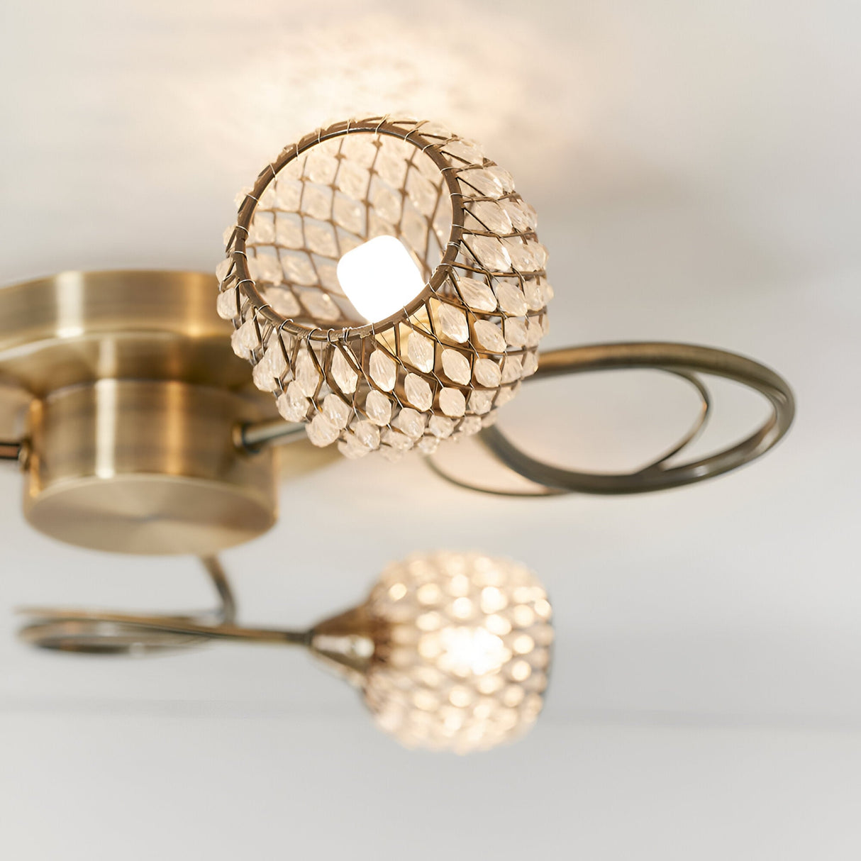 Endon Harcourt 3 light semi-flush ceiling light in antique brass, close-up of two beaded crystal globe shades on curved arms against a white ceiling.