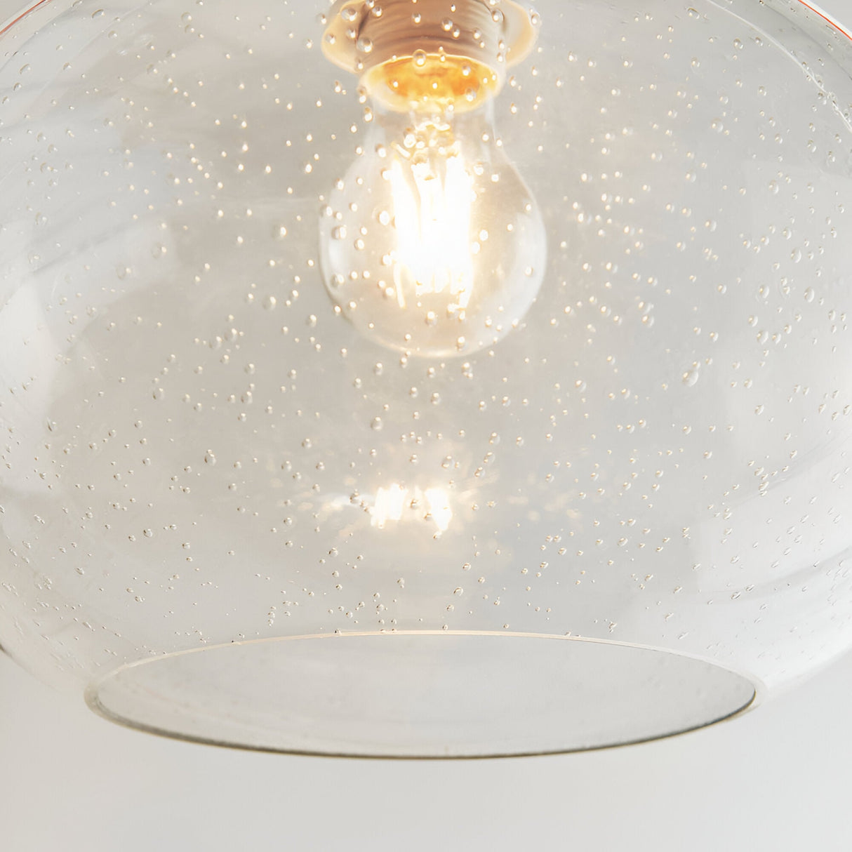 Close-up of the Endon Brackcombe clear bubble glass pendant shade, rounded open form, lit E27 filament bulb visible through the seeded glass.
