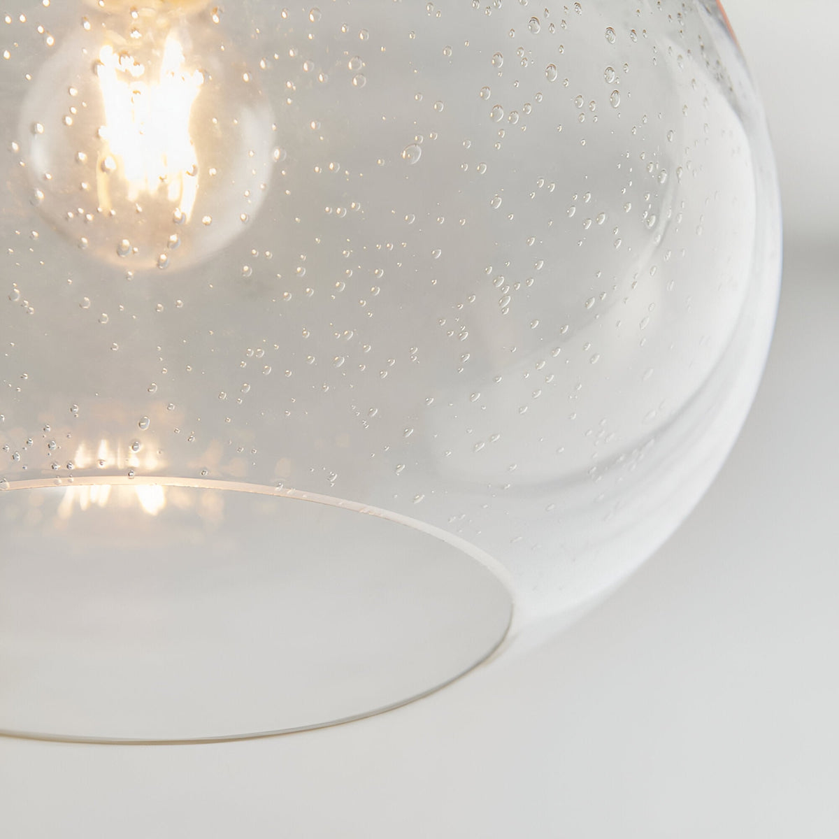 Close-up of the Endon Brackcombe clear bubble glass pendant shade with an illuminated E27 lamp glowing inside its rounded open form.