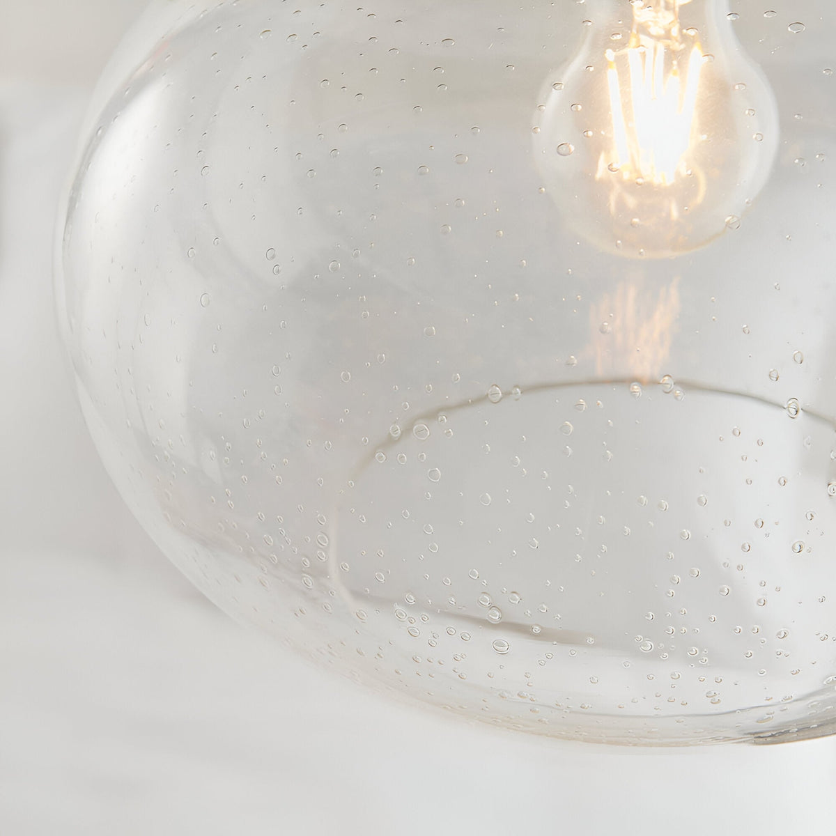 Close-up of Endon Brackcombe pendant shade in clear bubble glass with an exposed filament E27 lamp glowing inside.