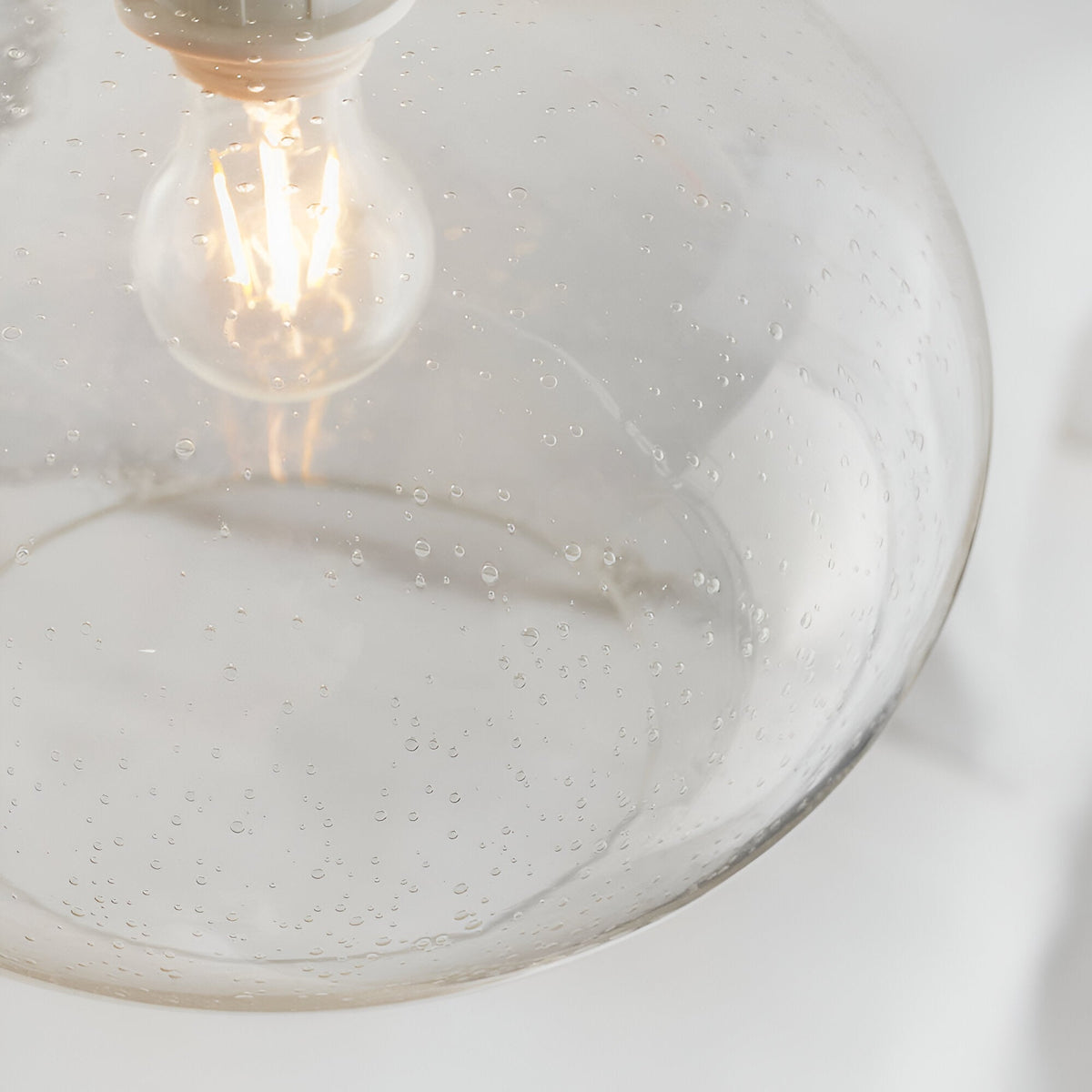 Close-up of the Endon Brackcombe clear bubble glass pendant shade with an exposed filament E27 lamp glowing inside the rounded globe.