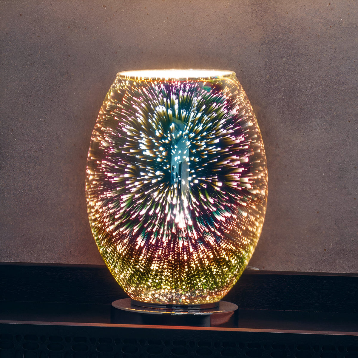 Endon Cliffwick touch table lamp illuminated on a dark shelf, showing its oval holographic glass body with a colourful firework burst effect on a chrome base.