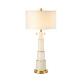 The Eloria 1 Light Stacked Alabaster Table Lamp features a brass and soft white tiered base, gold accents, and a white cylindrical shade, creating a modern and elegant look.
