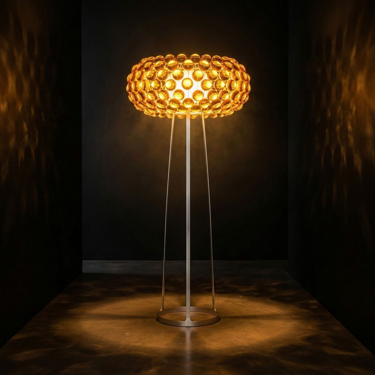 The Briller LED Floor Light - Gold features a circular honeycomb-patterned shade that emits warm, ambient light and casts intricate shadows across dark walls and floors.