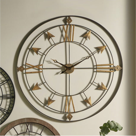 Graphite & Gold Iron Round Large Wall Clock, 120cm, with skeleton frame, gold Roman numerals and arrow markers, shown mounted on a light wall above a plant.