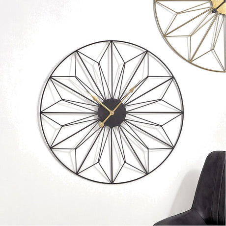 Black Iron Geo Design Round Wall Clock, 77cm, with an open geometric star pattern and gold hands, mounted on a white wall above a black chair.