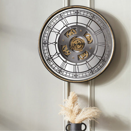 Round wall clock, 60cm, with mirrored face, Roman numerals, exposed gold cogs, and antique gold frame, shown on a light wall above a vase of dried grasses.