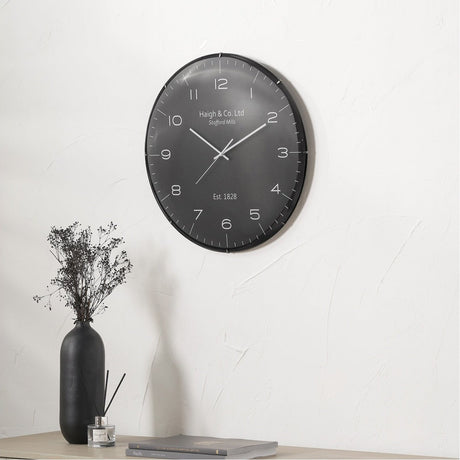 Black & Silver Dome Glass Wall Clock, 50cm, with black frame and grey face with silver numerals, mounted on a white wall above a table with a vase and books.