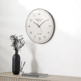 Round wall clock with a black frame and dome glass cover, cream dial with black numerals reading "Haigh & Co. Ltd", shown above a wooden sideboard styled with a black vase and books.