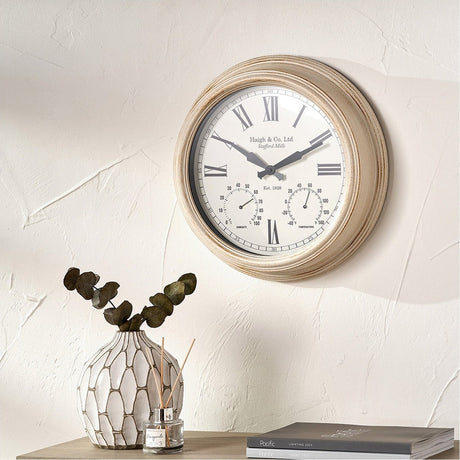 Antique effect gold brushed cream 42cm wall clock with Roman numerals and dual dials, shown mounted above a console table with a vase and books.