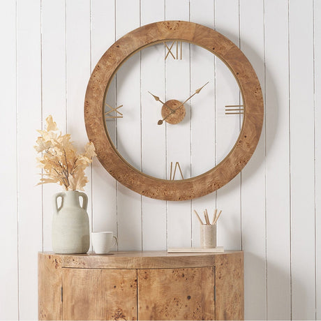 Newborough Burr Wood Effect Round Wall Clock, 80cm, with brass Roman numerals and hands, shown above a matching wood sideboard against white panelled wall.