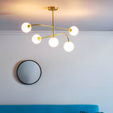 Endon Sinclair 5 light semi-flush ceiling light in brushed brass with white glass globes, installed above a round black-framed wall mirror in a living room.