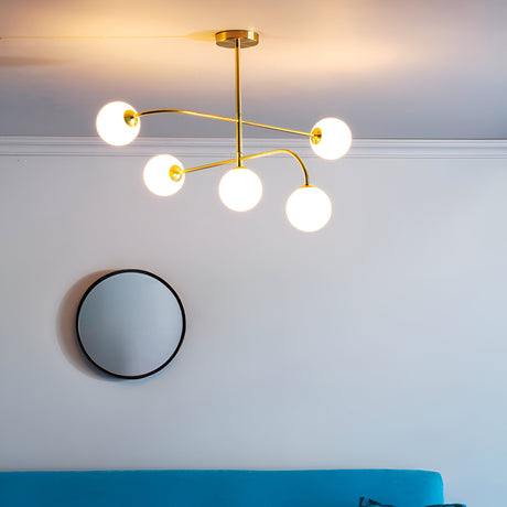 Endon Sinclair 5 light semi-flush ceiling light in brushed brass with white glass globes, installed above a round black-framed wall mirror in a living room.